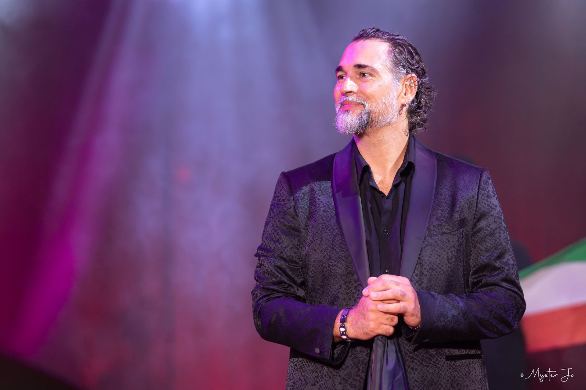 Nicolas Bouglione en smoking, mains jointes, saluant le public sous un faisceau lumineux